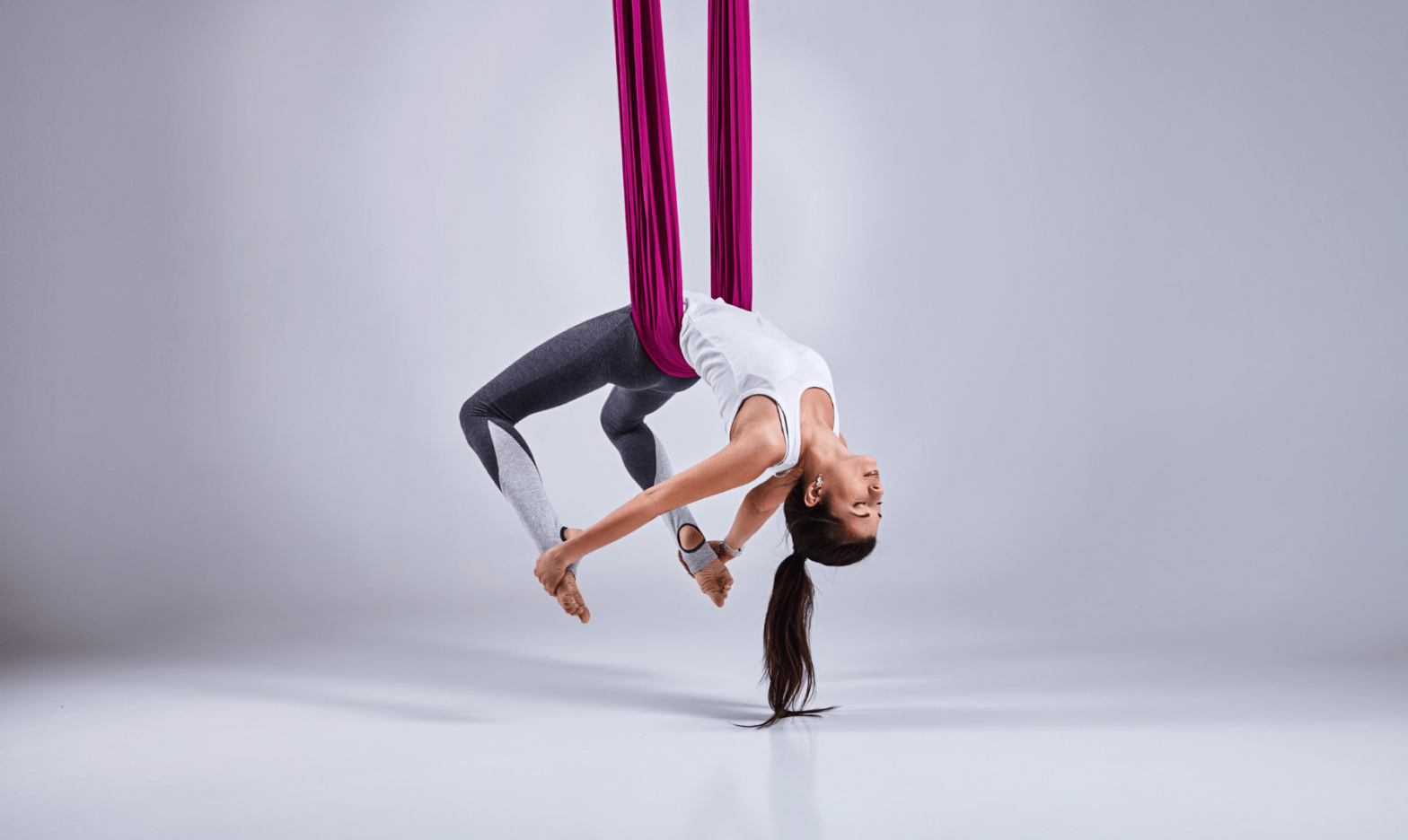 Femme yogiste de Fly Yoga suspendue par un ruban de couleur rose, tenant ses pieds avec ses mains