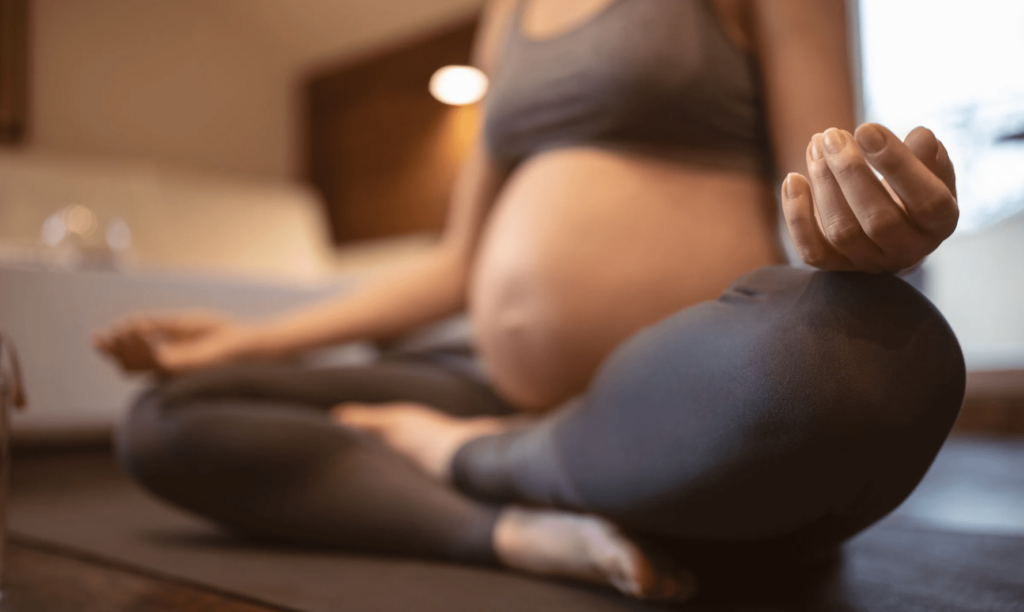 Femme enceinte assise sur son tapis de yoga, séance de Prénatal Yoga, position de méditation