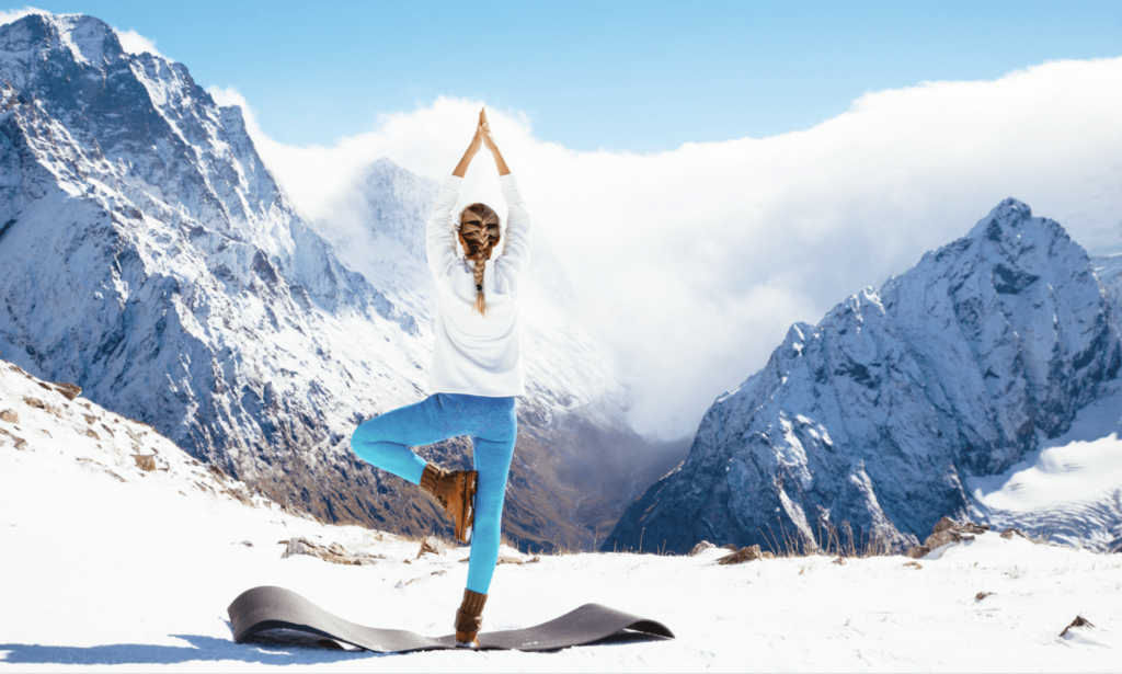 Femme debout, séance de Snowga Yoga, tapis de yoga, montagne enneigées en arrière plan