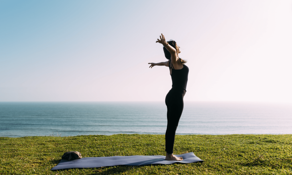 Séance de Yoga à Toulon - Femme debout sur gazon, séance de Vinyasa Yoga, tapis de yoga, mer calme avec vague en arrière plan