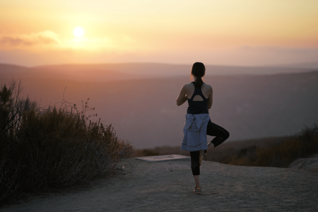 Femme effectuant la pose de yoga viksasana devant le coucher du soleil