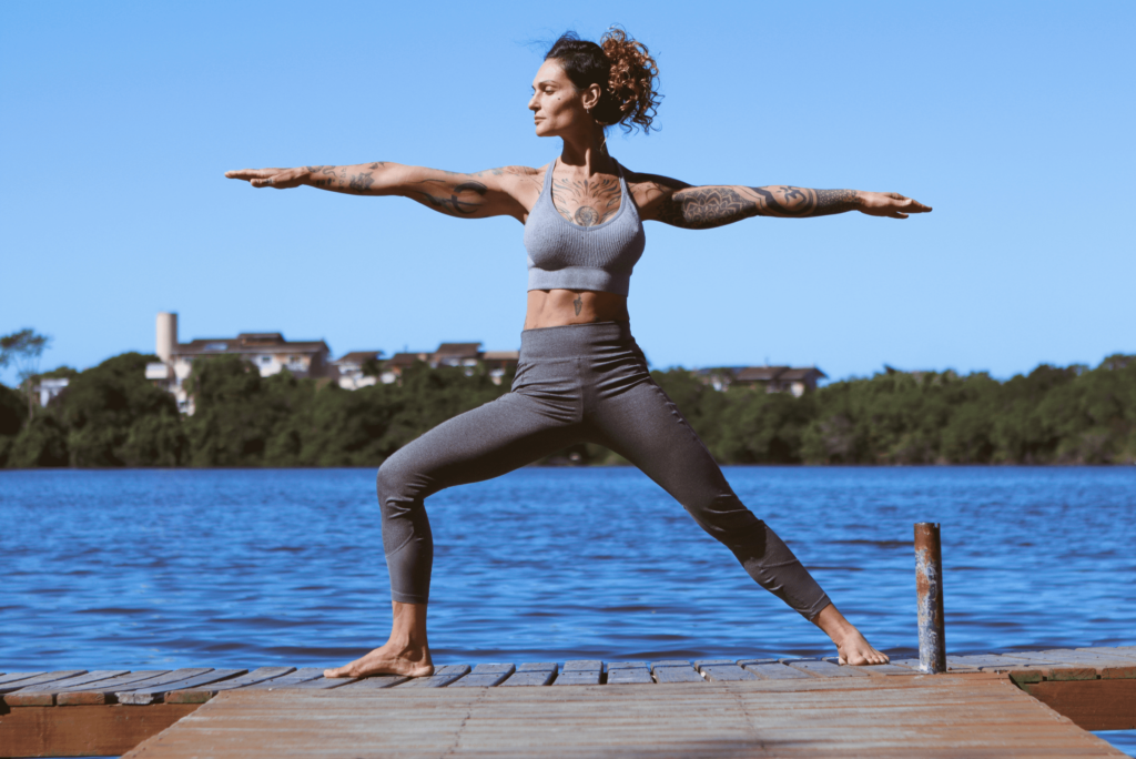 Jeune femme effectuant le asana : posture du guerrier sur un ponton devant la mer