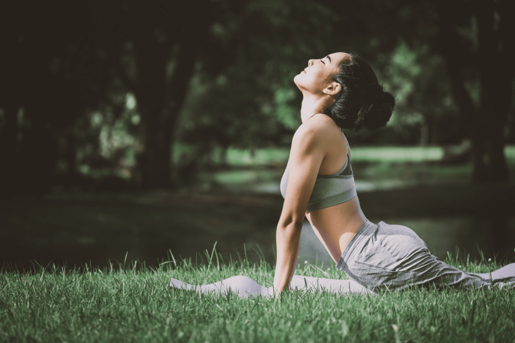 Jeune femme en posture du cobra (bhujangasana) sur un tapis de yoga dans un parc