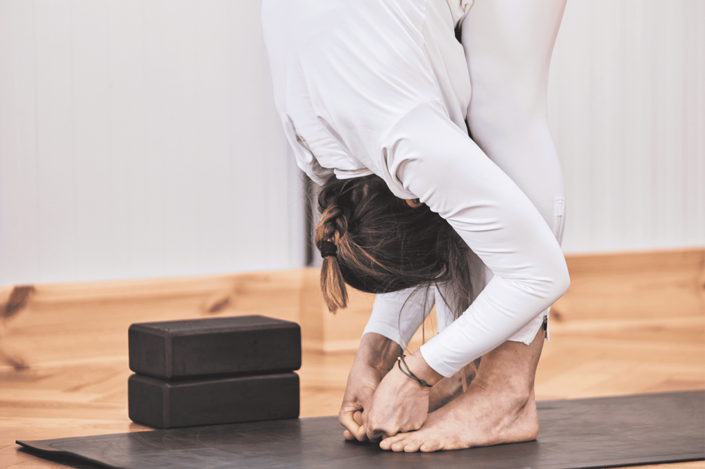 Femme en posture des mains aux orteils sur un tapis de yoga noir.