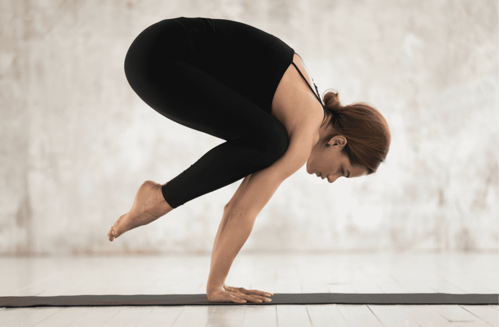 Femme effectuant la posture de la grue (Bakasana) dans un studio de yoga.