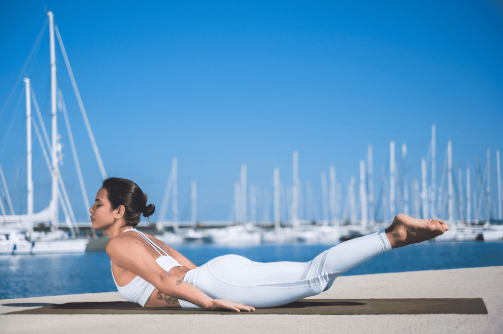 Femme en posture de la sauterelle devant un port, sur un tapis de yoga.