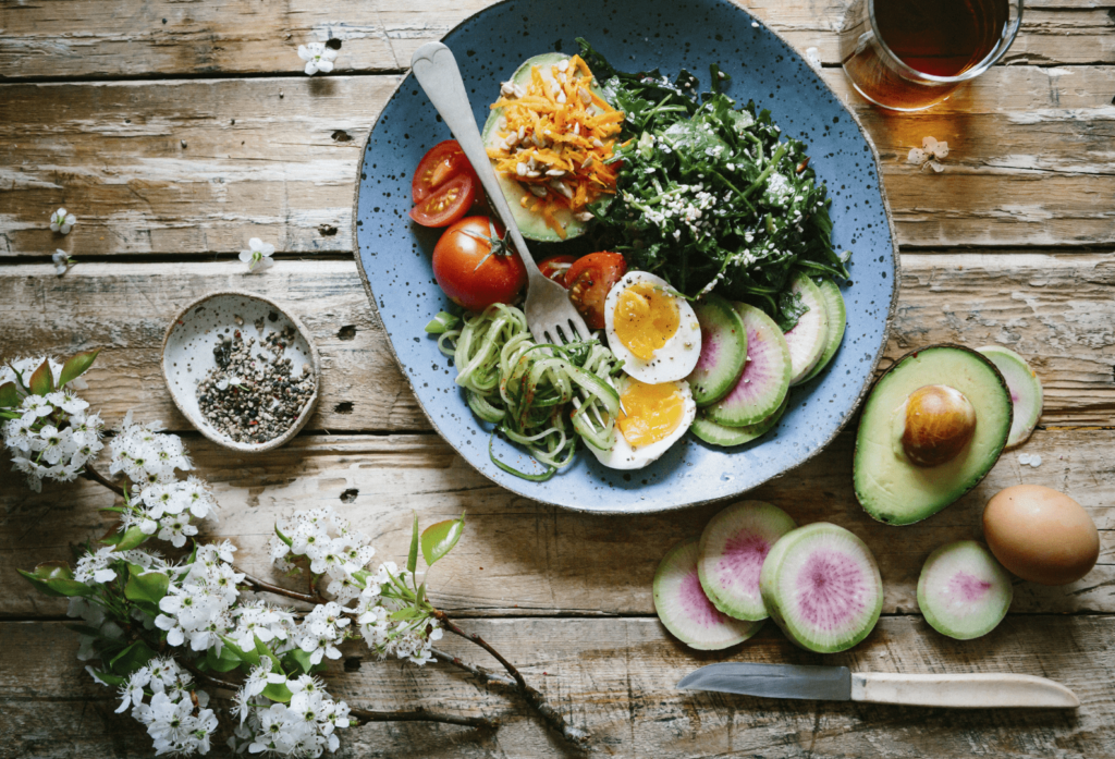 Salade équilibrée avec avocat, œufs, radis, tomates et verdure dans une assiette sur une table en bois.