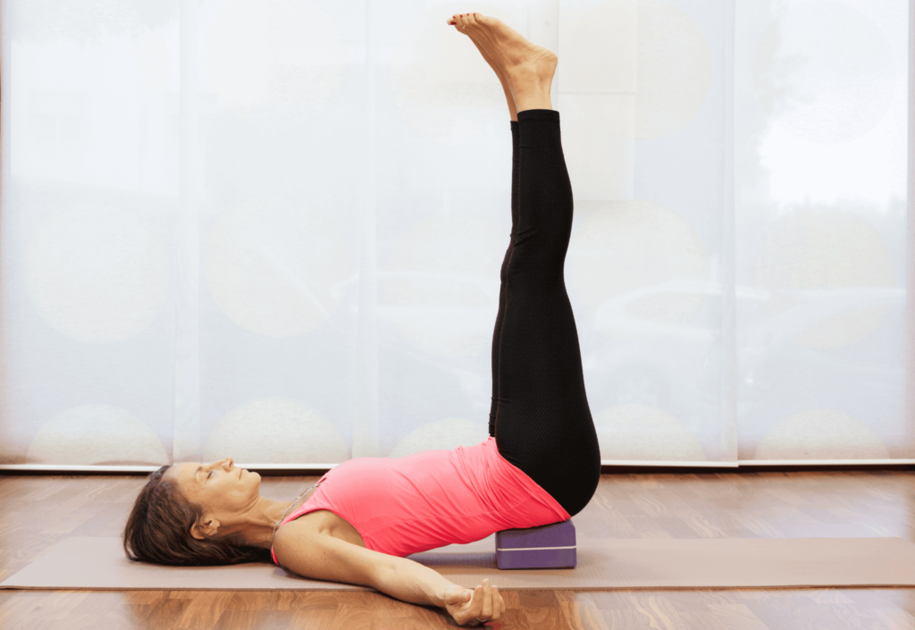 Femme en pose des jambes contre le mur avec un bloc de yoga.