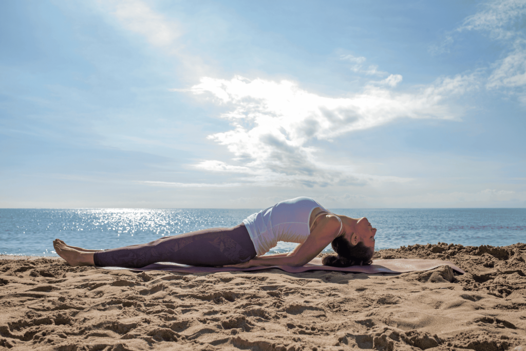 Femme en posture du poisson soutenu devant la mer, sur un tapis de yoga rose.