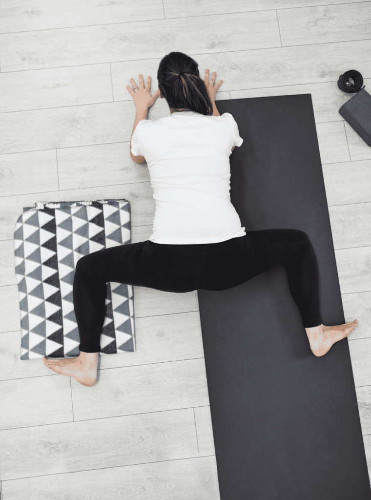 Femme en posture de la grenouille sur un tapis de yoga noir.