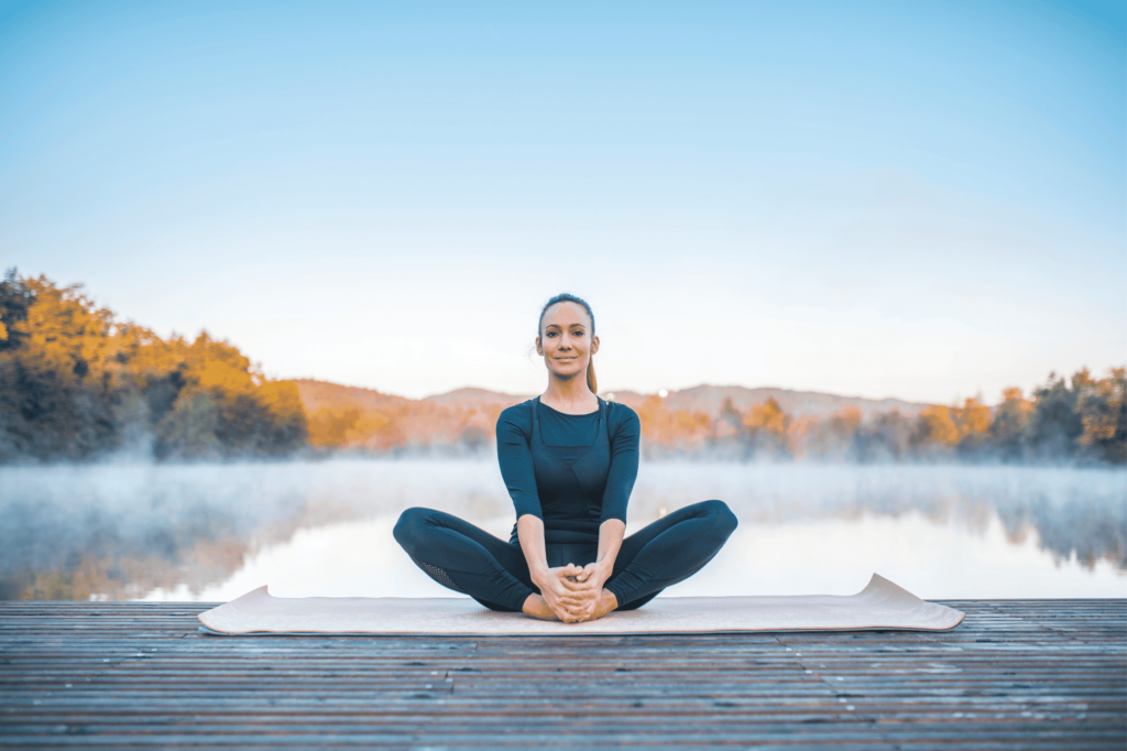 Femme en pose du papillon sur un ponton devant un lac.