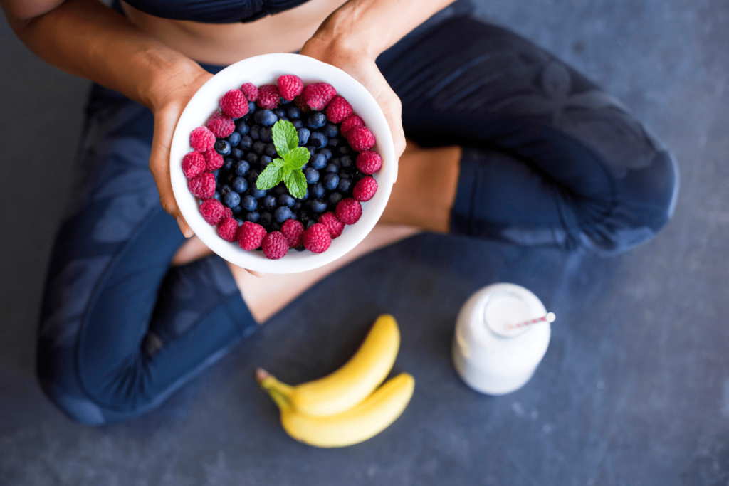 Personne tenant un bol de baies fraîches, entouré de bananes et de lait, après une séance de yoga.