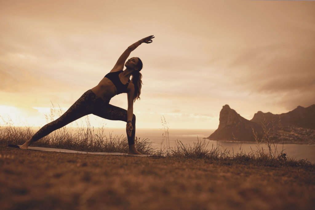 Femme en angle latéral étendu devant un coucher de soleil.