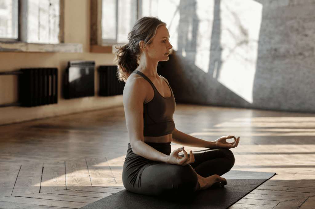 Femme en pleine méditation assise sur son tapis de yoga dans un studio calme et minimaliste.