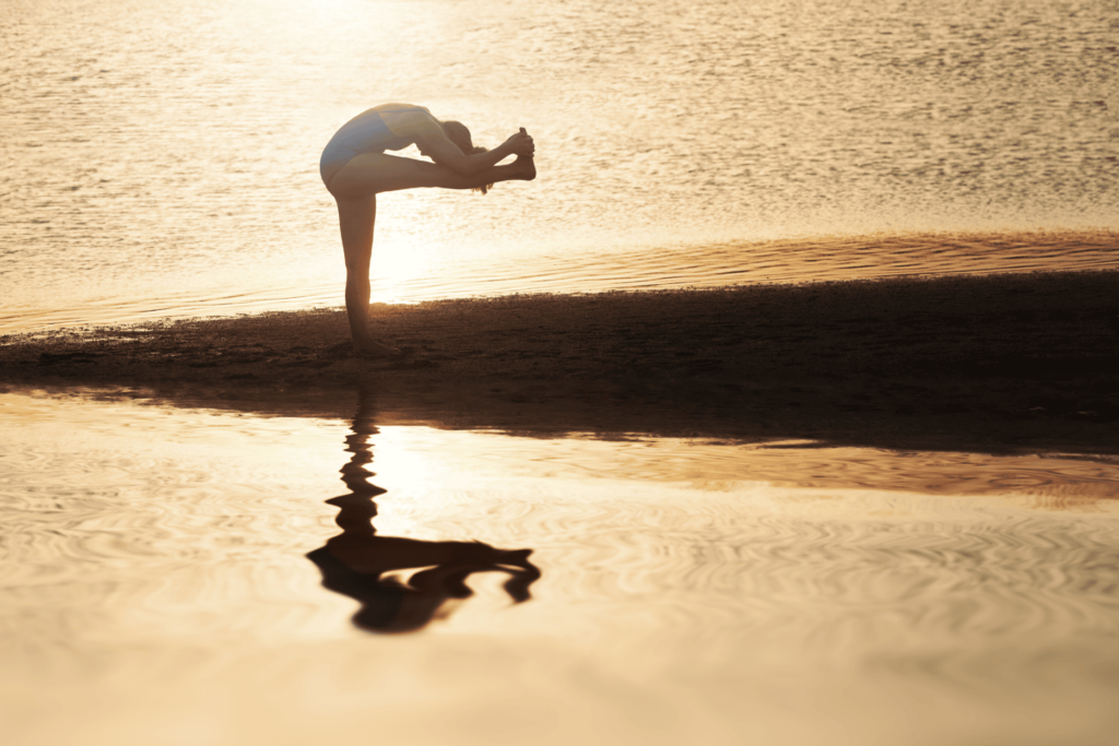 Femme en position front au genou debout sur une plage, devant un coucher de soleil.