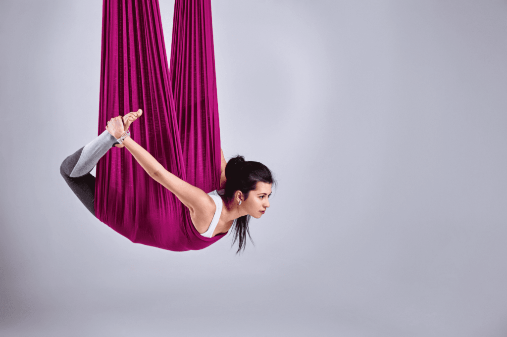 Femme pratiquant une séance de yoga aérien dans un hamac rose suspendu.