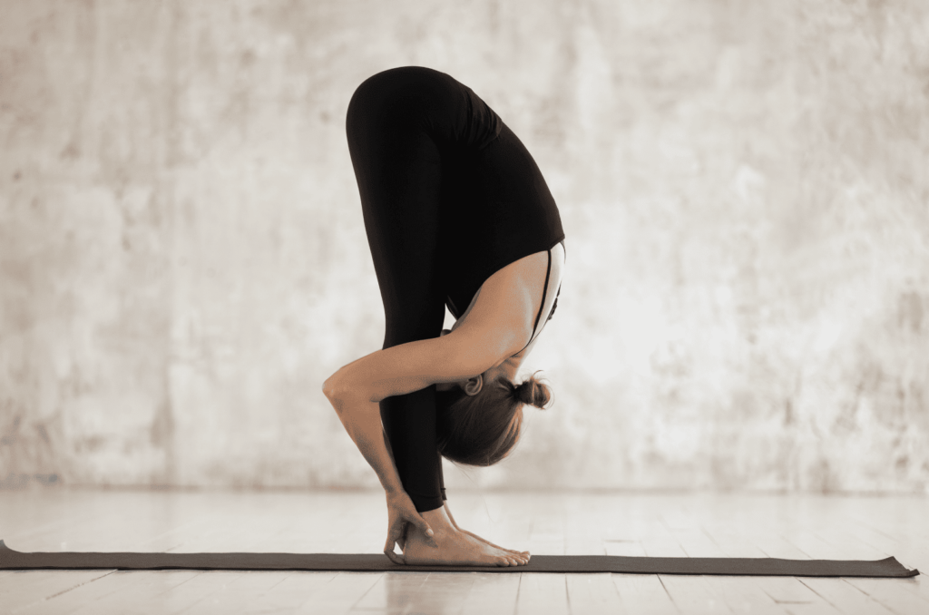 Femme penchée vers l'avant en position debout dans un studio de yoga lumineux.