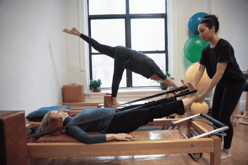 Deux séniors utilisant une machine reformer avec un coach de pilates.