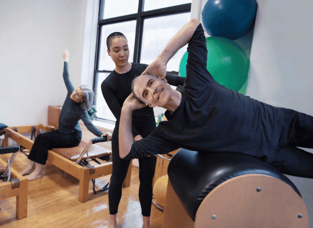 Deux séniors pratiquant le pilates sur reformer avec un entraîneur.